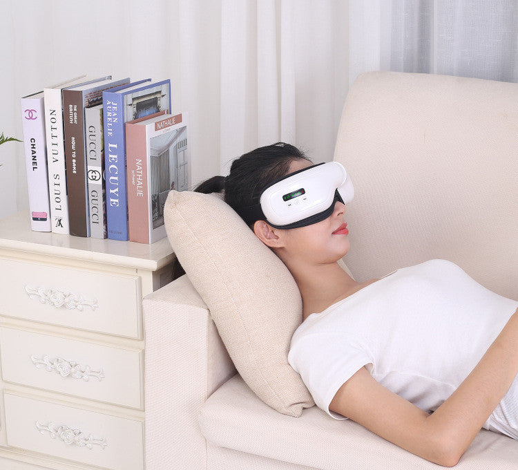Woman relaxing with Smart Bluetooth Eye Massager while lying on a couch with books nearby