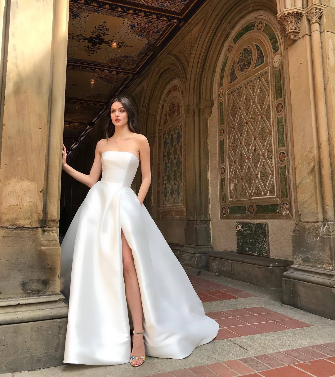 Elegant woman in a white bandeau high waist dress with a side slit, posing in a historic setting